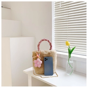 Sac seau en peluche avec poignée tressée rose et chaîne à côté d'un téléphone