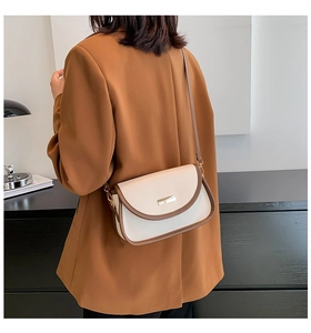 Detail of cream crossbody bag with brown trim and gold buckle worn on a brown blazer