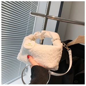 Detail of white plush handbag featuring a ruffled leather handle and gold hardware