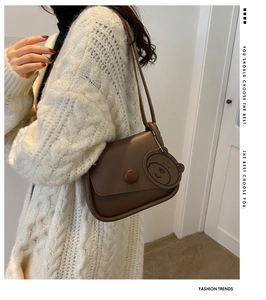 Detail view of a brown leather shoulder bag with a bear charm on a white sweater