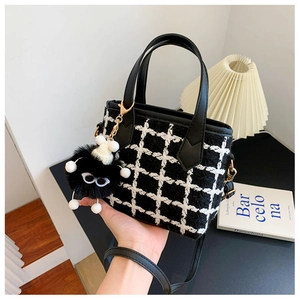 Detail of tweed bucket bag with black leather handle and unique monster charm accessory