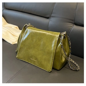 Detail of olive green glossy leather bag with vintage bronze chain on a dark sofa