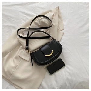 Détail du sac de selle en cuir noir avec boucle dorée en demi-lune et bandoulière fine