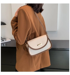 Detail of a retro cream shoulder bag with brown piping worn by a model in a cozy room