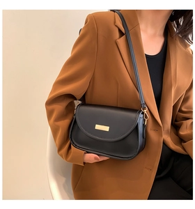Detail of minimalist black leather crossbody bag with gold metal hardware on model