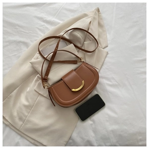 Sacoche marron sur tissu blanc avec blazer et téléphone pour comparer la taille du sac
