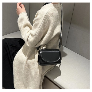Detail of a minimalist black leather shoulder bag with decorative white topstitching