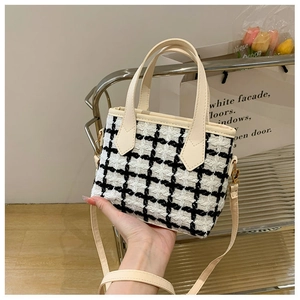 Close-up of black and white tweed bucket bag with cream leather strap and metal hooks