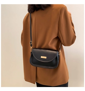 Back view of black leather crossbody bag with gold buckle on a brown blazer model