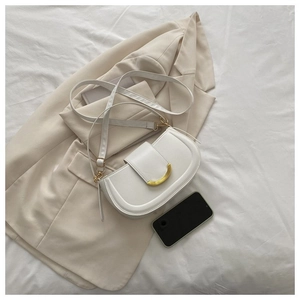 Gros plan d'un sac besace blanc avec boucle dorée sur fond minimaliste beige et noir