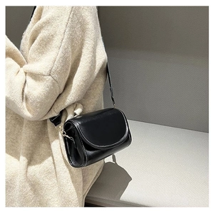 Detail of a black leather saddle bag featuring contrasting white stitching and gold hardware