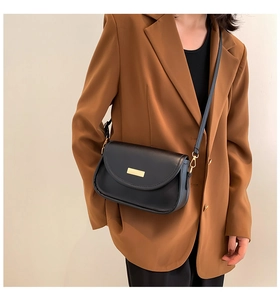 Detail of a black leather crossbody bag with a gold buckle on a caramel blazer outfit