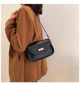 Detailed side view of black matte leather crossbody bag with gold buckle on model