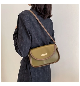 Detail of vintage olive green crossbody bag with brown trim and gold buckle worn with navy suit