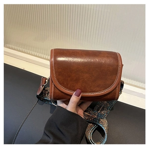 Detail of dark brown crossbody bag featuring contrast stitching and colorful woven strap
