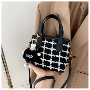 Close-up of houndstooth tweed bucket bag with plush monster charm and faux leather handle