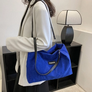Blue corduroy tote bag with black leather straps shown on a model in a modern interior
