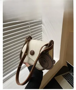 Detail of a vintage cream and coffee crossbody bag with round buckle and bear charm