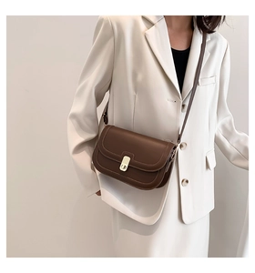 Detail of a brown leather saddle bag with a golden metal buckle on a white blazer