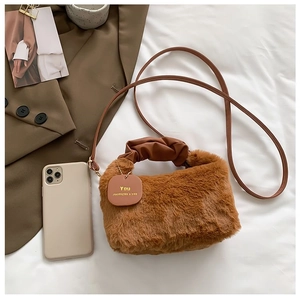 Detail of plush caramel faux fur tote with pleated leather handles on white bedding