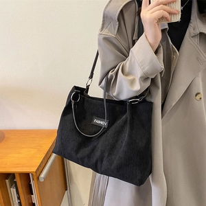 Black corduroy tote bag with Fashion label shown on a model in a minimalist room