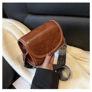 Macro shot of vintage brown crossbody bag with white stitching and ethnic print strap