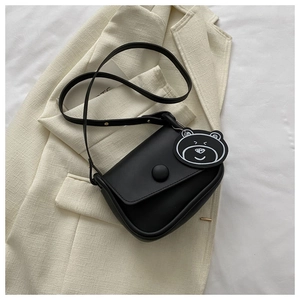 Detailed shot of matte black saddle bag with decorative round buckle and bear charm