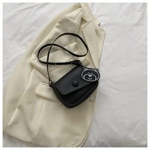 Close-up of black matte crossbody square bag with a cute bear tag on a beige blazer