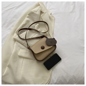 Detail shot of mini crossbody bag with bear charm placed on a beige blazer with a phone