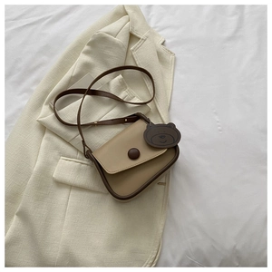 Detail of light brown crossbody bag with bear charm on a beige blazer background