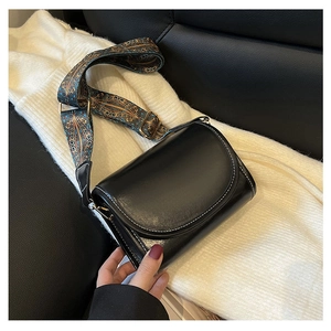 Detail of black faux leather crossbody bag with vintage ethnic patterned wide shoulder strap