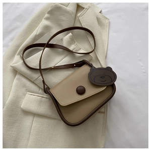 Detail of a beige flap crossbody bag with brown trim and cute bear charm on a blazer