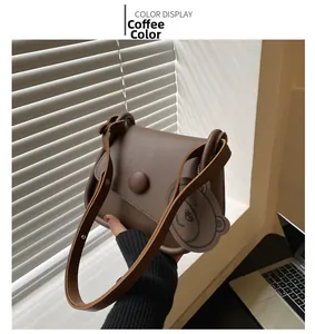 Detail of coffee brown crossbody bag with round buckle and cute bear pendant charm