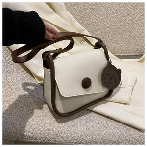 Detail view of cream PU leather crossbody bag with brown trim and cute bear charm