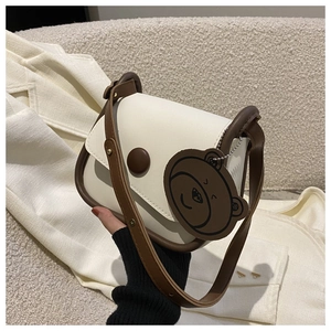 Close-up of cream leather crossbody bag with brown trim and cute bear charm pendant