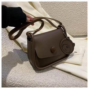 Detail of dark brown leather crossbody bag with decorative buckle and cute bear charm