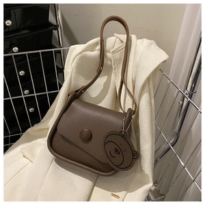 Detail of dark brown leather shoulder bag featuring a large button closure and bear charm