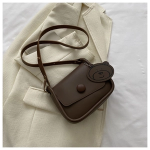 Detail of dark brown matte square bag with round button and cute bear tag on tweed fabric