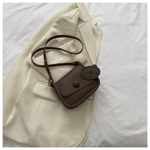 Detail of dark brown leather crossbody bag with a cute bear head pendant on beige blazer