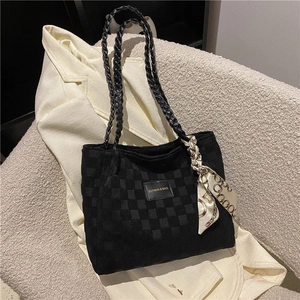 Black checkerboard tote bag with woven handles and silk scarf on a beige sofa