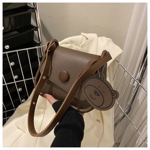 Close-up of brown crossbody bag with a matte leather texture and a cute bear charm