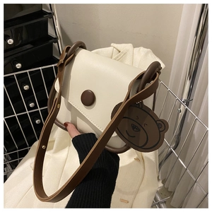 Detail of cream shoulder bag with brown trim and cute bear charm in hand-held display