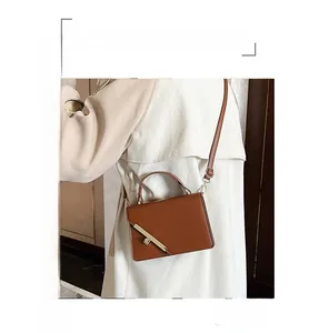 Detail of a brown textured crossbody bag featuring a sleek diagonal gold metal lock clasp
