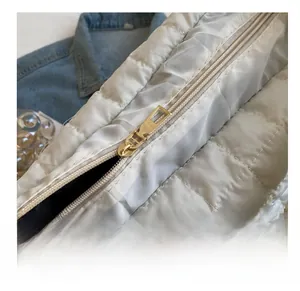 Detail of smooth gold zipper and quilted fabric on a light grey puffer shoulder bag