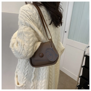 Close-up of a brown leather shoulder bag with a decorative round buckle and blue bear charm