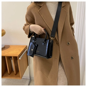 Detailed view of black glossy handbag with wide shoulder strap and mini hanging pouch
