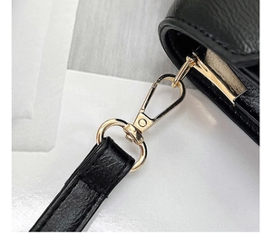 Detailed close-up of golden metal lobster clasp on black lychee grain leather handbag