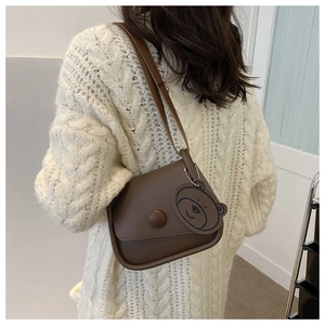 Close-up of brown crossbody bag with a cute bear charm and round buckle detail