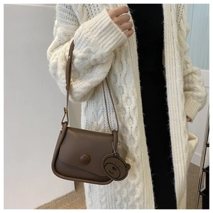 Detail of dark brown leather crossbody bag with wave edge flap and cute bear pendant