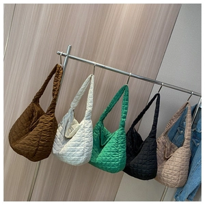 Quilted tote bags in five colors displayed on metal hangers against a wooden wall